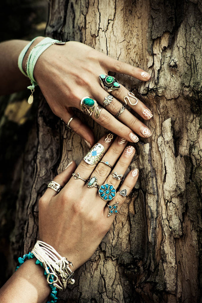 primer plano de las manos de la mujer en la superficie del árbol con una gran cantidad de joyas de estilo boho, anillos y pulseras al aire libre día de verano
 - Foto, Imagen