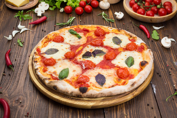 rústica pizza italiana Margarita com mussarela, tomate cereja e folhas de manjericão sobre fundo de madeira
 - Foto, Imagem