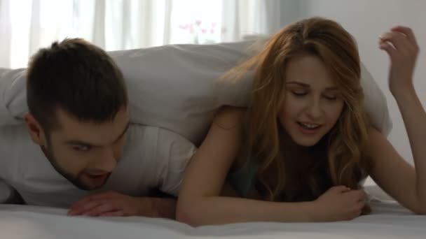 Happy lovers getting out from under blanket in bed, newlyweds on honeymoon, love - Video, Çekim
