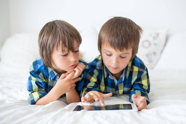 Two preschool children, boy brothers, playing at home in bed on tablet - Foto, afbeelding