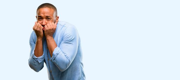 Afrikanisch-amerikanischer Mann mit Bart verängstigt und nervös ausdrückende Angst und Panik Geste, überwältigt isoliert vor blauem Hintergrund - Foto, Bild