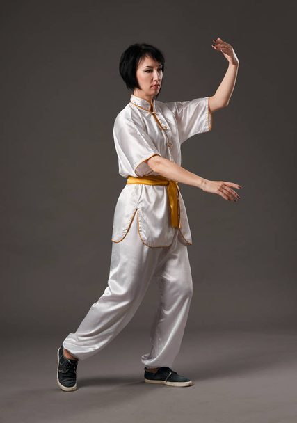 Young woman practicing tai chi chuan. Chinese management skill Qi's energy. Gray background, studio shoot. - Foto, Imagen
