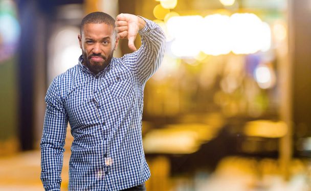 African american man met baard duim omlaag ongelukkig teken van afkeer, negatieve expressie en afkeuring nachts tonen - Foto, afbeelding