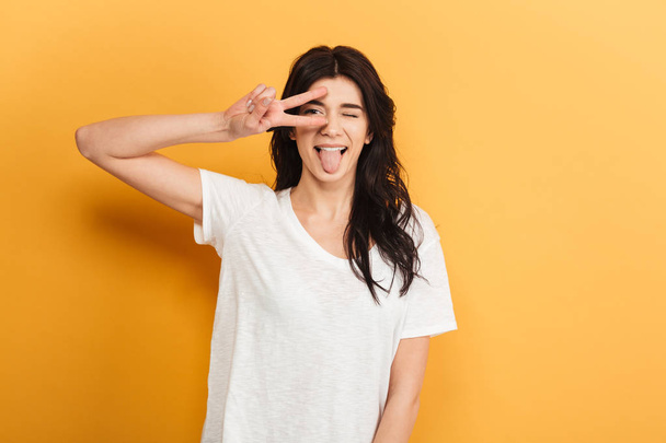 Image of cute young pretty lady standing isolated over yellow background looking camera showing tongue having fun. - Photo, image