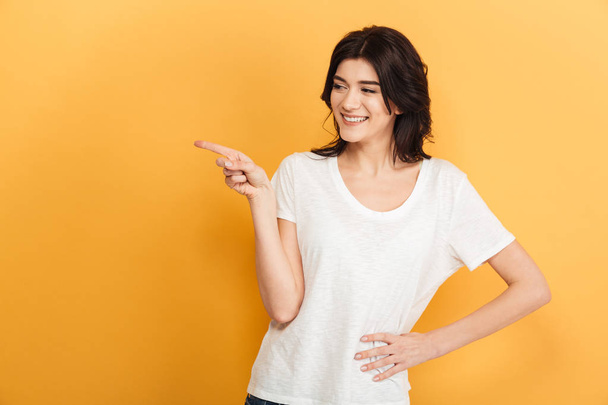 Photo of young emotional woman standing isolated over yellow background looking aside pointing. - Photo, Image
