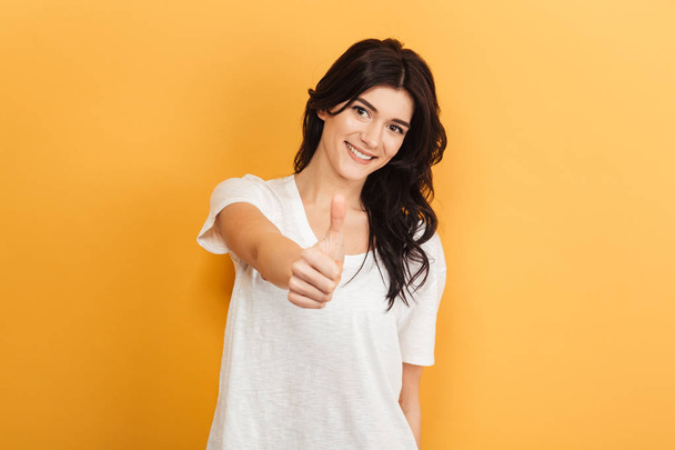 Image of beautiful young lady standing isolated over yellow background looking camera showing thumbs up gesture. - Foto, immagini