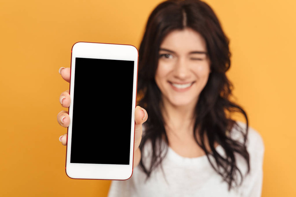 Image of young pretty woman standing isolated over yellow background looking camera showing display of mobile phone. - Photo, Image