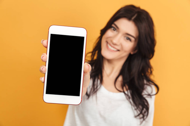 Image of young pretty woman standing isolated over yellow background looking camera showing display of mobile phone. - Zdjęcie, obraz