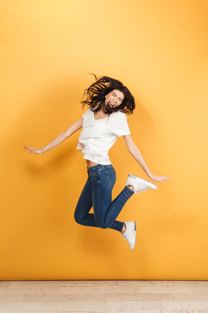 Image of young screaming emotional woman jumping isolated over yellow background. - Foto, immagini