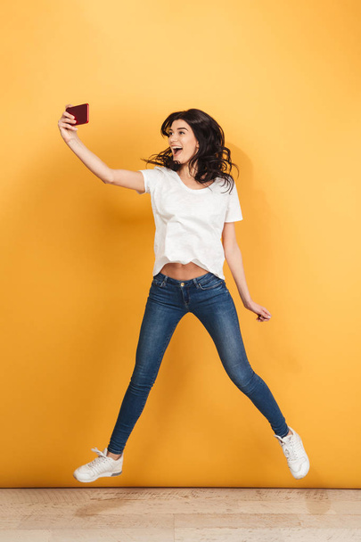 Image of cute young pretty woman jumping isolated over yellow background make selfie by phone. - 写真・画像