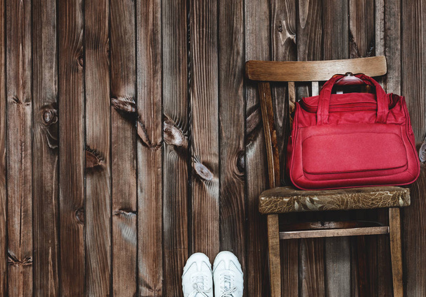 punainen matkakassi seisoo vanhalla tuolilla, ruskealla taustalla
 - Valokuva, kuva