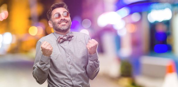 Hombre de mediana edad, con barba y pajarita feliz y emocionado celebrando la victoria expresando gran éxito, poder, energía y emociones positivas. Celebra el nuevo trabajo alegre en el club nocturno
 - Foto, imagen