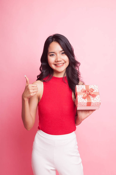 Asian woman thumbs up with a gift box on pink background - Foto, Imagen