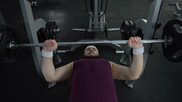 Chubby man unable to lift heavy barbell in gym during sport exercise, health - Filmmaterial, Video