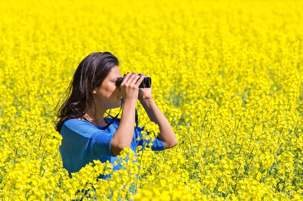 Fiatal nő távcső a virágzó sárga Repce field nézegette - Fotó, kép