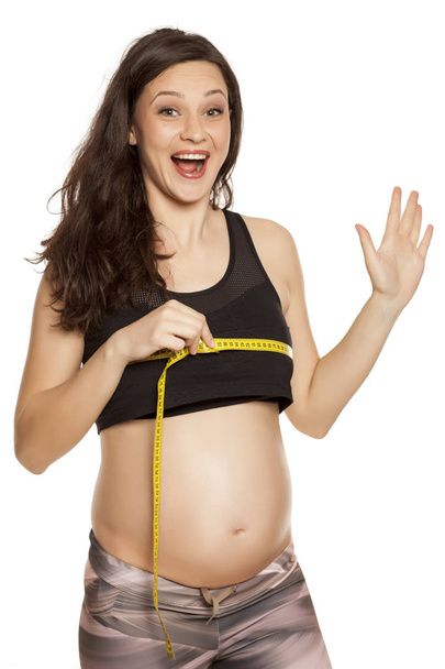 Щаслива вагітна жінка вимірює груди на білому тлі
 - Фото, зображення