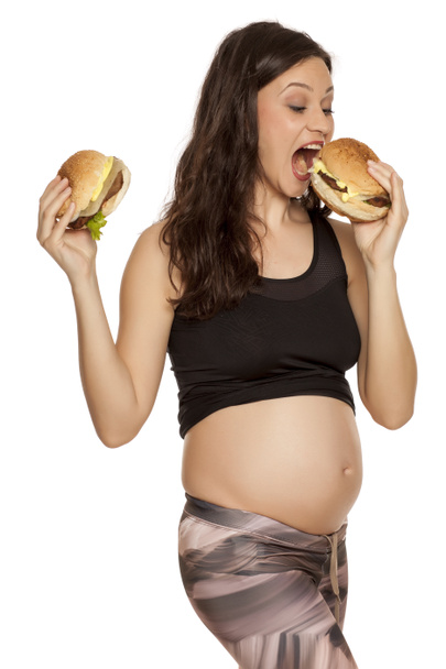 Young pregnant greedy woman holding two burgers on a white background - Foto, afbeelding