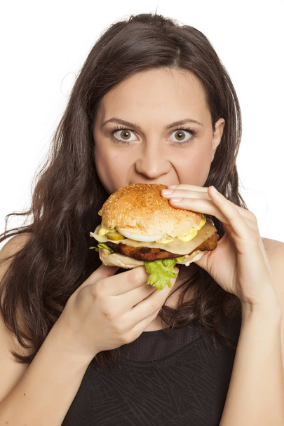 Jovem bela mulher gananciosa comendo hambúrguer em um fundo branco
 - Foto, Imagem