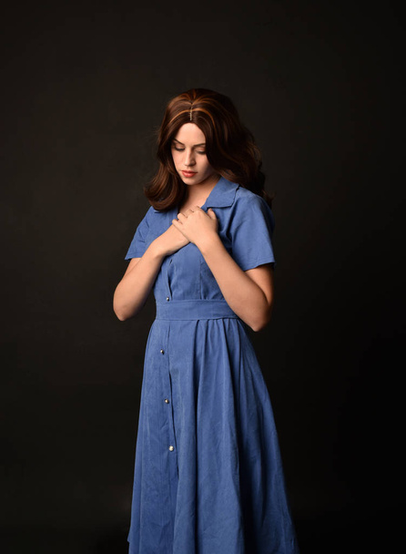 3/4 portrait of brunette lady wearing blue dress. posed on black studio background. - Фото, зображення