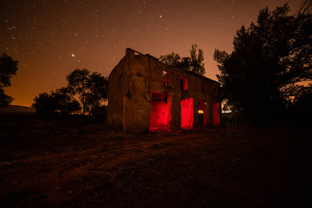Fotografía de larga exposición en una casa abandonada e iluminada en su interior en color rojo
. - Foto, Imagen