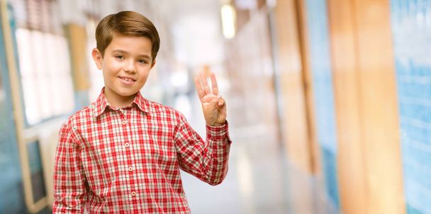 Όμορφος νήπιο παιδί με πράσινα μάτια, αυξάνοντας το δάχτυλο, είναι ο αριθμός τρία στο διάδρομο του σχολείου - Φωτογραφία, εικόνα