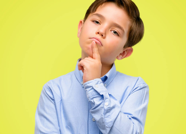 Handsome toddler child with green eyes doubt expression, confuse and wonder concept, uncertain future over yellow background - Photo, Image