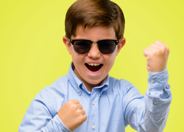 Handsome toddler child with green eyes happy and excited celebrating victory expressing big success, power, energy and positive emotions. Celebrates new job joyful over yellow background - Photo, Image