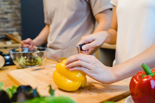 Woman hands cutting bell pepper in the kitchen. Beautiful happy asian couple are cooking in the kitchen. Young asian couple have romantic time while staying at home. Couple lifestyle at home concept. - Fotó, kép