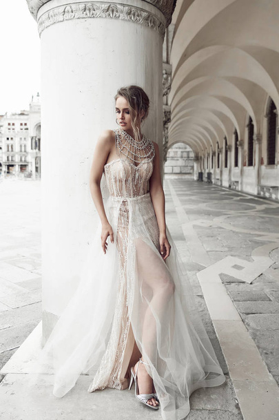 Beautiful bride in elegant, luxury ivory dress and updo hairstyle, posing near column in Venice, Italy - Фото, изображение