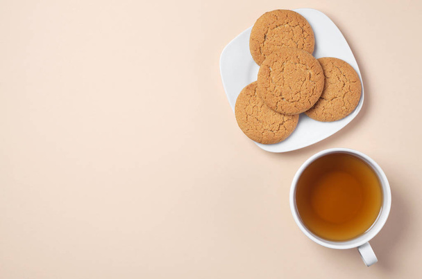 Oatmeal cookies in plate and cup of tea on light brown background, top view with space for text - Photo, Image