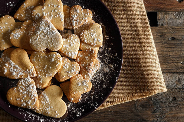 Deliziosi biscotti fatti in casa a forma di cuore spruzzati con zucchero a velo su sacco e tavole di legno. Immagine orizzontale vista dall'alto
. - Foto, immagini