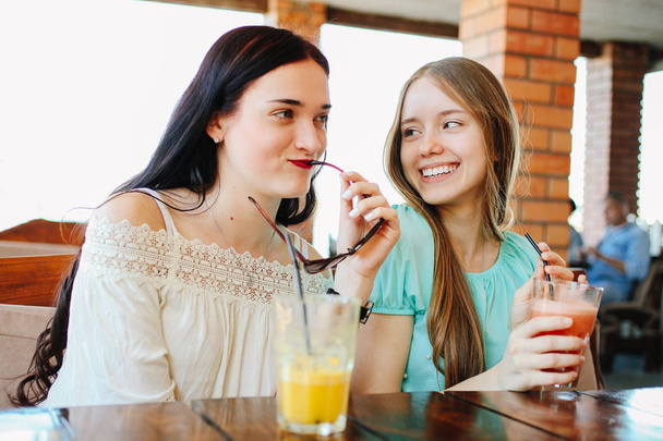 2 つの美しい女の子は、カフェで新鮮なフルーツのスムージーを飲んでいます。. - 写真・画像