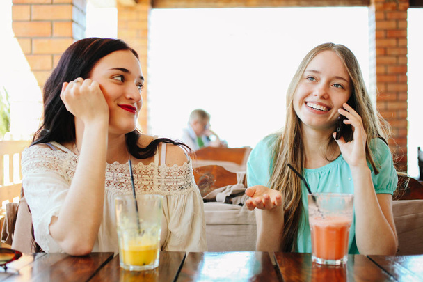 İki güzel kız bir kafede oturan ve taze meyve smoothies içme. - Fotoğraf, Görsel