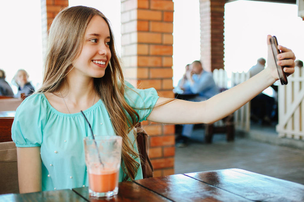 Beautiful girl doing selfie with fruit smoothies in a cafe. - Zdjęcie, obraz