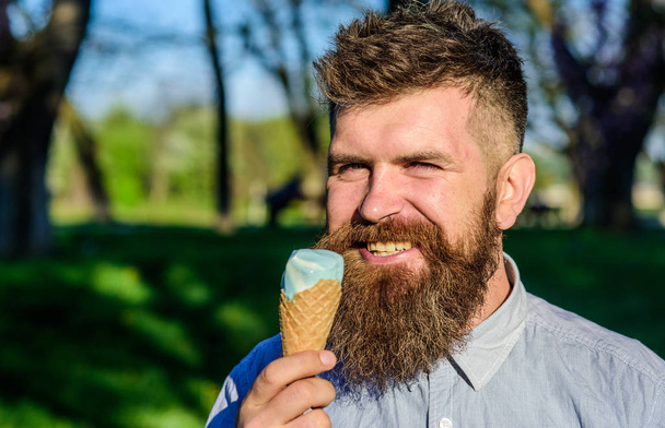 Man with long beard enjoy ice cream, close up. Chilling concept. Man with beard and mustache on happy face eats ice cream, nature background, defocused. Bearded man with ice cream cone - Valokuva, kuva