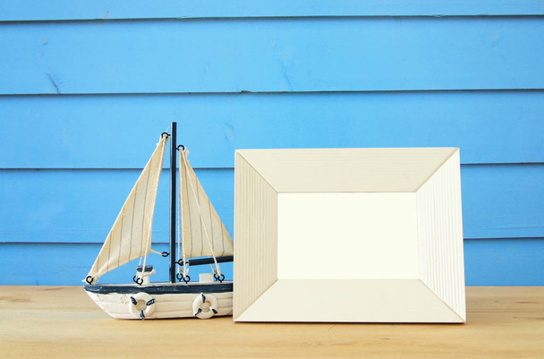 Nautical concept with empty photo frame and sail boat over wooden table. For photography montage - Φωτογραφία, εικόνα
