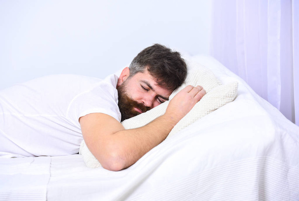 Man in shirt laying on bed, white wall on background. Guy on calm face sleeping on white sheets and pillow. Macho with beard and mustache sleeping, relaxing, having nap, rest. Nap and siesta concept - Photo, Image