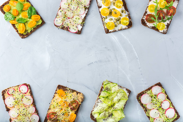 Їжа та напої, концепція натюрморту. Різноманітні бутерброди ручної роботи з вершковим сиром, гумусом, авокадо, овочами та мікрозеленими паростками на обідній стіл. Вид зверху плоский простір копіювання фону
 - Фото, зображення