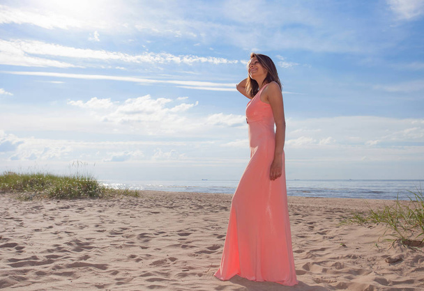 Beautiful woman in pink dress on sandy beach of Baltic sea. - Photo, Image