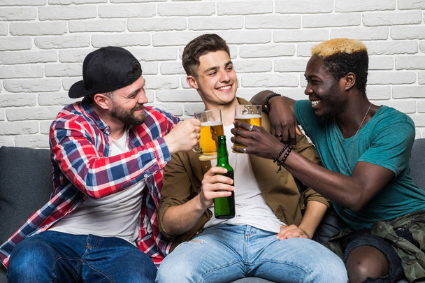 Close up portrait of attractive, stylish, cheerful men holding bottles with lager in hands, watching soccer word cup competition, cheering for favorite team - Photo, Image