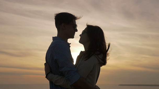 Young people hug each other passionately on the Black Sea shore at sunset                                 Profile of a charming young woman embracing her romantic sweetheart on the Black Sea shore at idyllic sunset with a sparkling sun path in summer - Footage, Video
