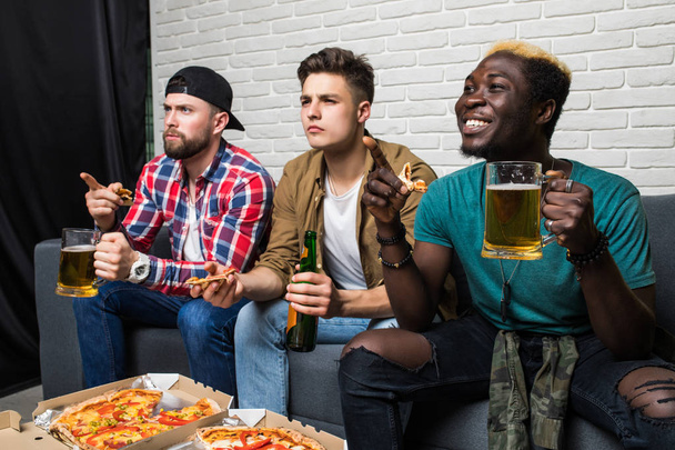 Profilbild einer Gruppe von drei männlichen Freunden, die sich ein Fußballspiel im Fernsehen anschauen, während sie Bier trinken und Pizza essen - Foto, Bild