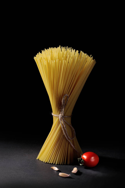 Pacote de macarrão espaguete com alho e tomate cereja em um fundo preto
. - Foto, Imagem