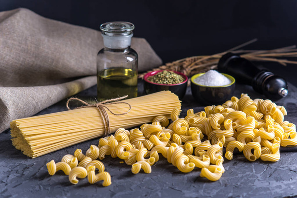 Kypsentämätön italialainen pasta spagetti ja ainesosat ruoanlaittoon keittiössä tummalla pohjalla. Elintarvikemuotoilun koostumuksen käsite
. - Valokuva, kuva