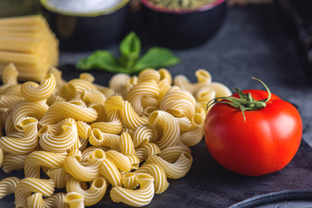 Неприготовленная итальянская паста каватаппи и спагетти с ингредиентами для томатного соуса на тёмном фоне. Концепция композиции пищевого дизайна
. - Фото, изображение
