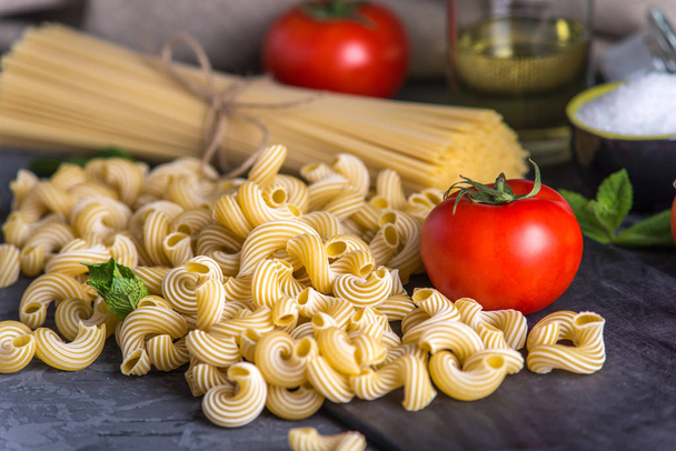Pastas italianas sin cocer cavatappi y espaguetis con ingredientes para salsa de tomate sobre un fondo oscuro. El concepto de la composición del diseño de alimentos
. - Foto, imagen