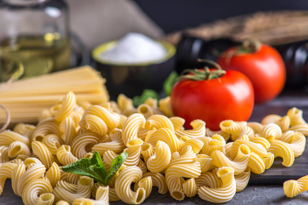 Kypsentämätön italialainen pasta cavatappi ja spagetti, jossa on tomaattikastikkeen ainesosia tummalla pohjalla. Elintarvikemuotoilun koostumuksen käsite
. - Valokuva, kuva