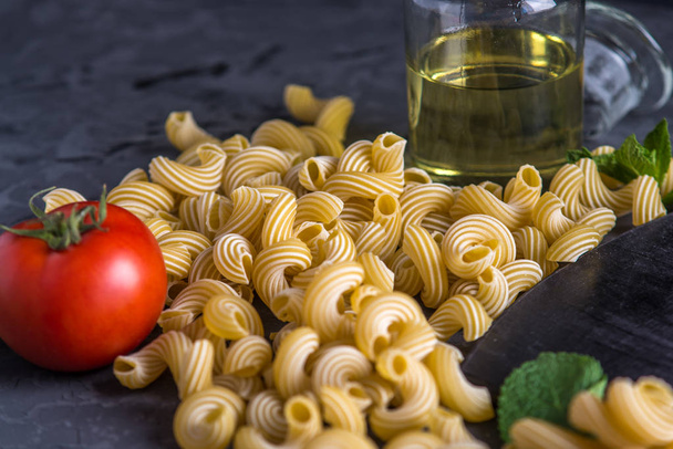 Kypsentämätön italialainen pasta cavatappi, jossa on tomaattikastikkeen ainesosia tummalla pohjalla. Elintarvikemuotoilun koostumuksen käsite
. - Valokuva, kuva
