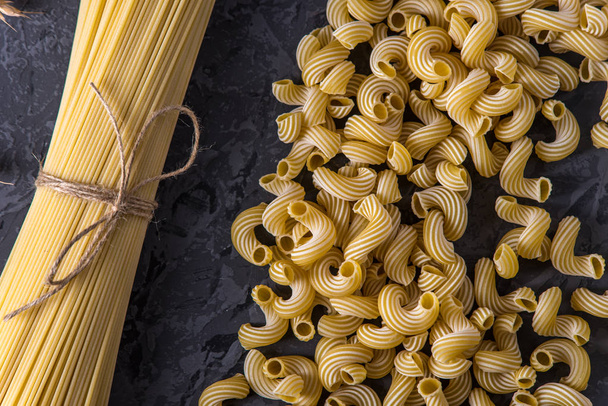 Uncooked italian pasta spaghetti and cavatappi with spikelets of durum wheat on a dark background. The concept of the composition of food design. - Photo, Image