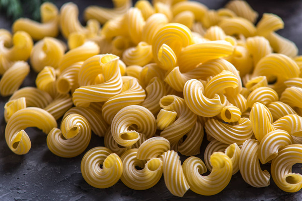 Kypsentämättömät italialaiset pastat spiraalien muodossa tummalla taustalla. Elintarvikkeiden koostumuksen käsite
. - Valokuva, kuva